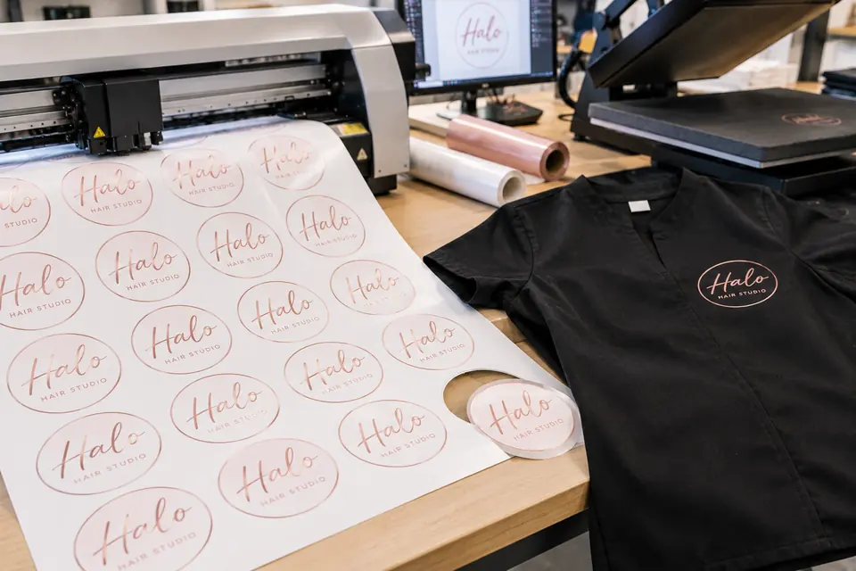 Sheet of contour-cut hair salon logo transfers beside a pressed black tunic